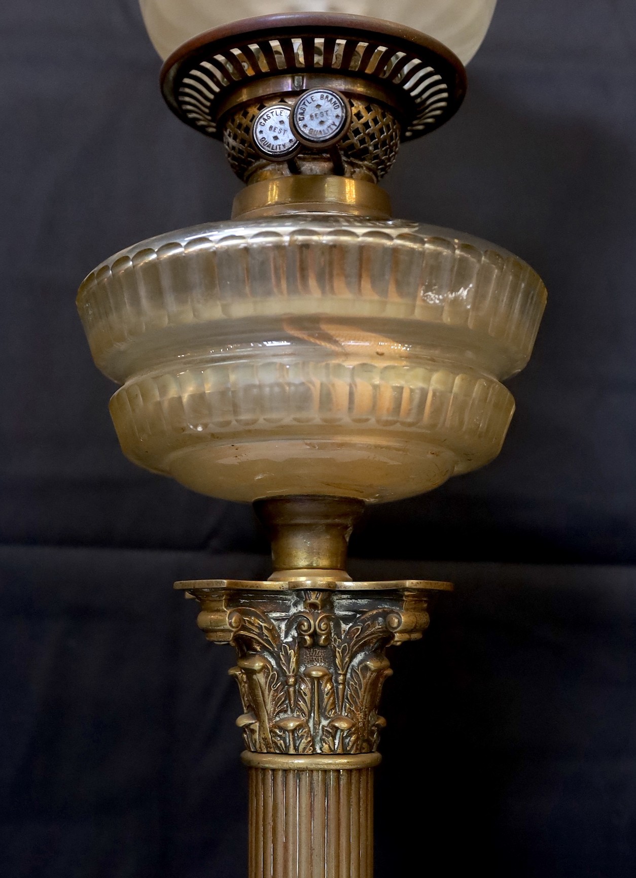 An Edwardian brass Corinthian column oil lamp with cut glass reservoir, Castle Brand mechanism and etched glass shade, height overall 86cm.